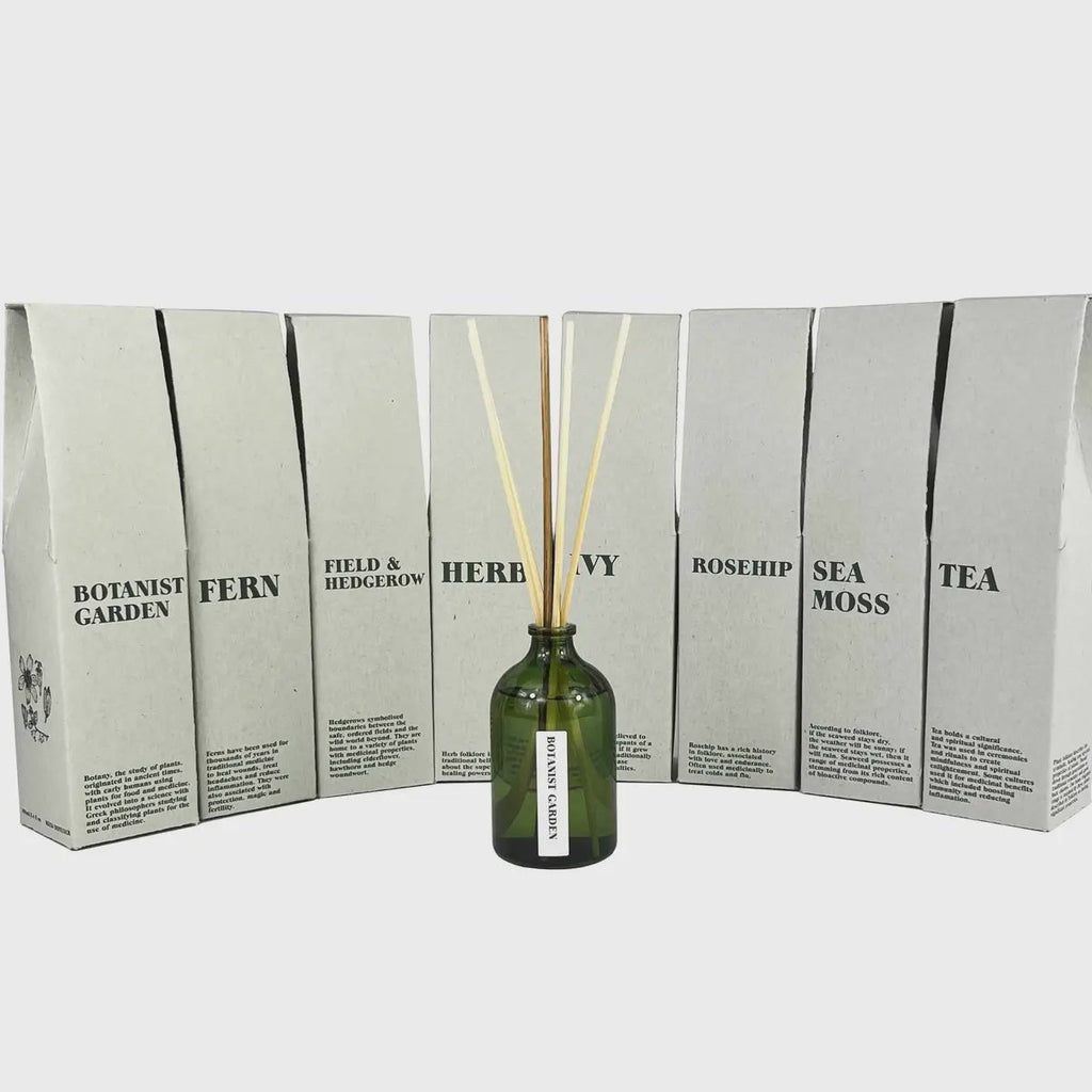 Green bottle with diffuser sticks in front of a display box with text on a white background