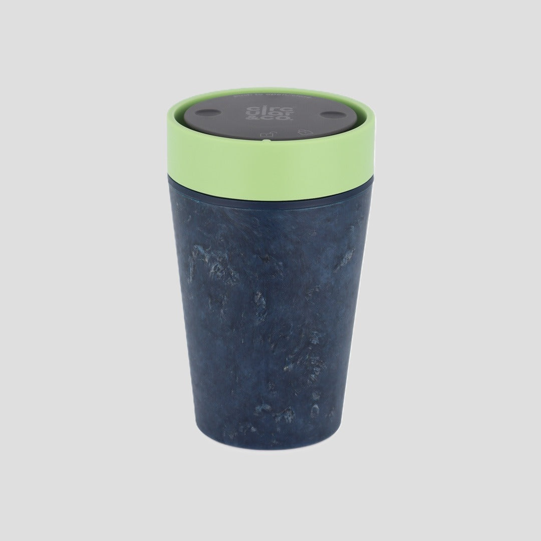 A reusable travel tumbler with a dark navy blue textured body and a light green lid, shown on a solid light gray background.