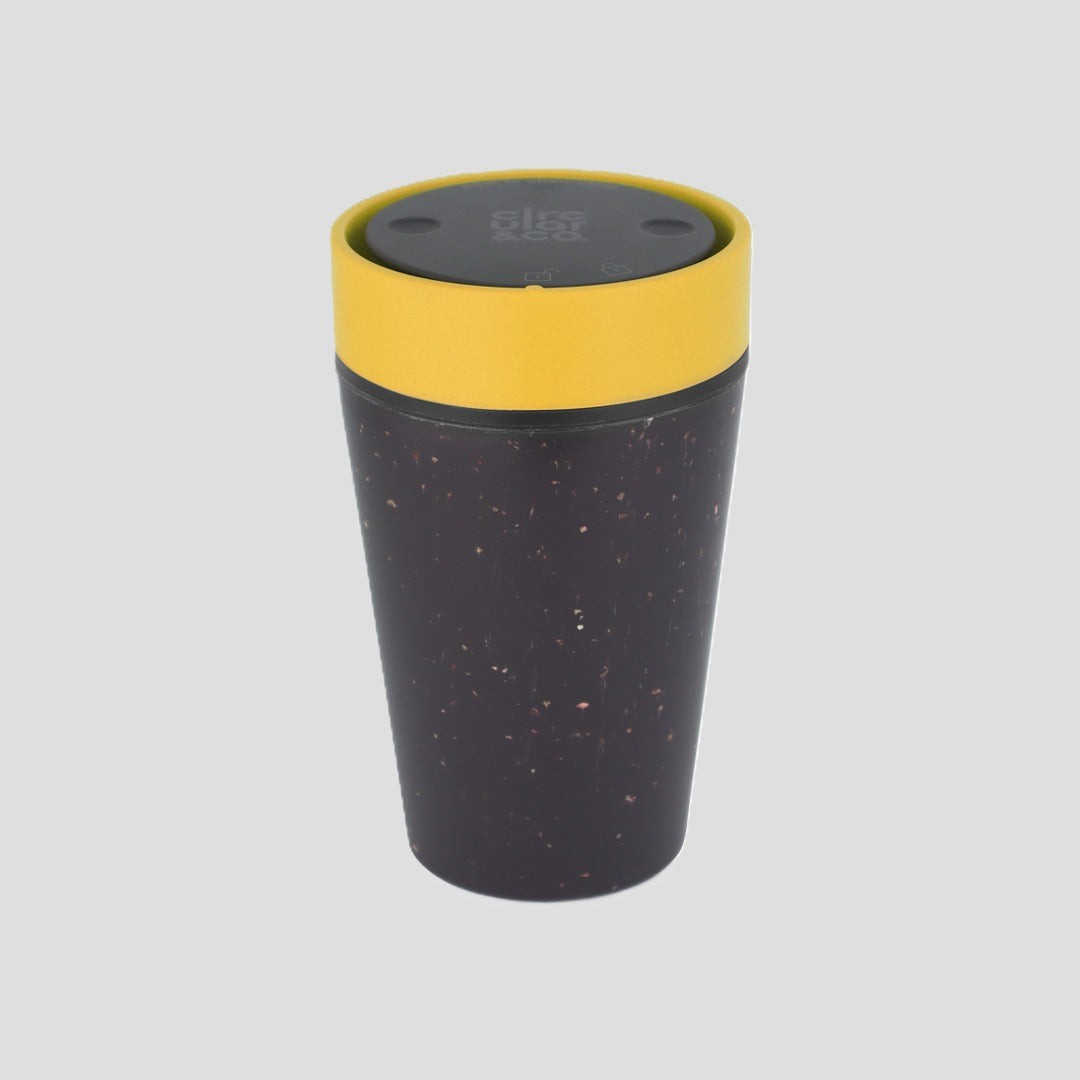 A reusable insulated tumbler with a dark speckled body, a bright yellow band around the upper portion, and a dark gray lid, shown on a solid light gray background.