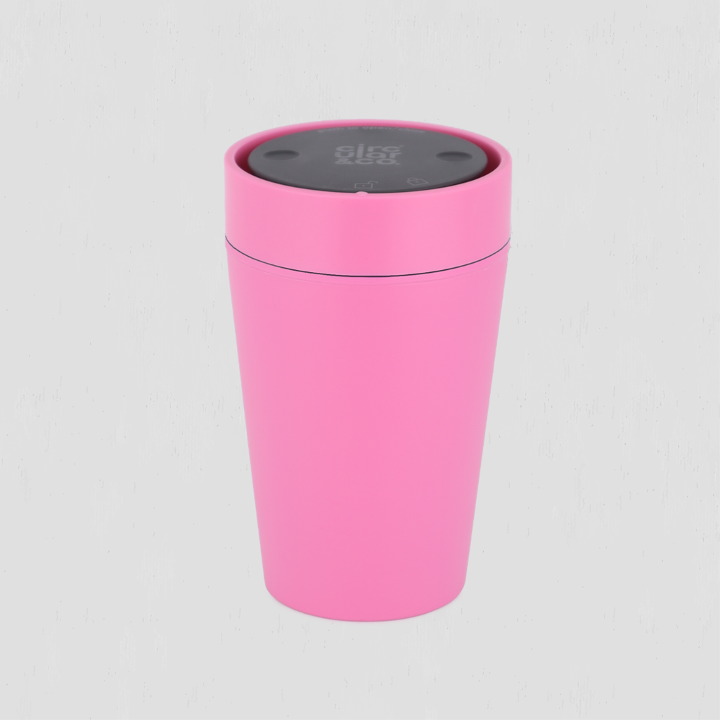 A pink cylindrical reusable coffee cup with a dark gray top lid, shown on a light gray background.