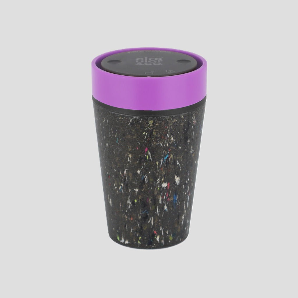 A reusable insulated tumbler with a black and multicolor speckled exterior and a bright purple lid, shown on a solid light gray background.
