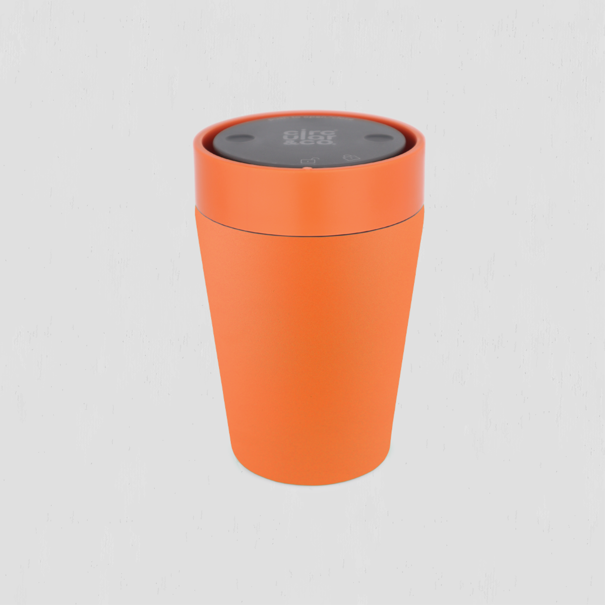 An orange cylindrical cup or container with a dark gray lid, shown on a light gray background. 
