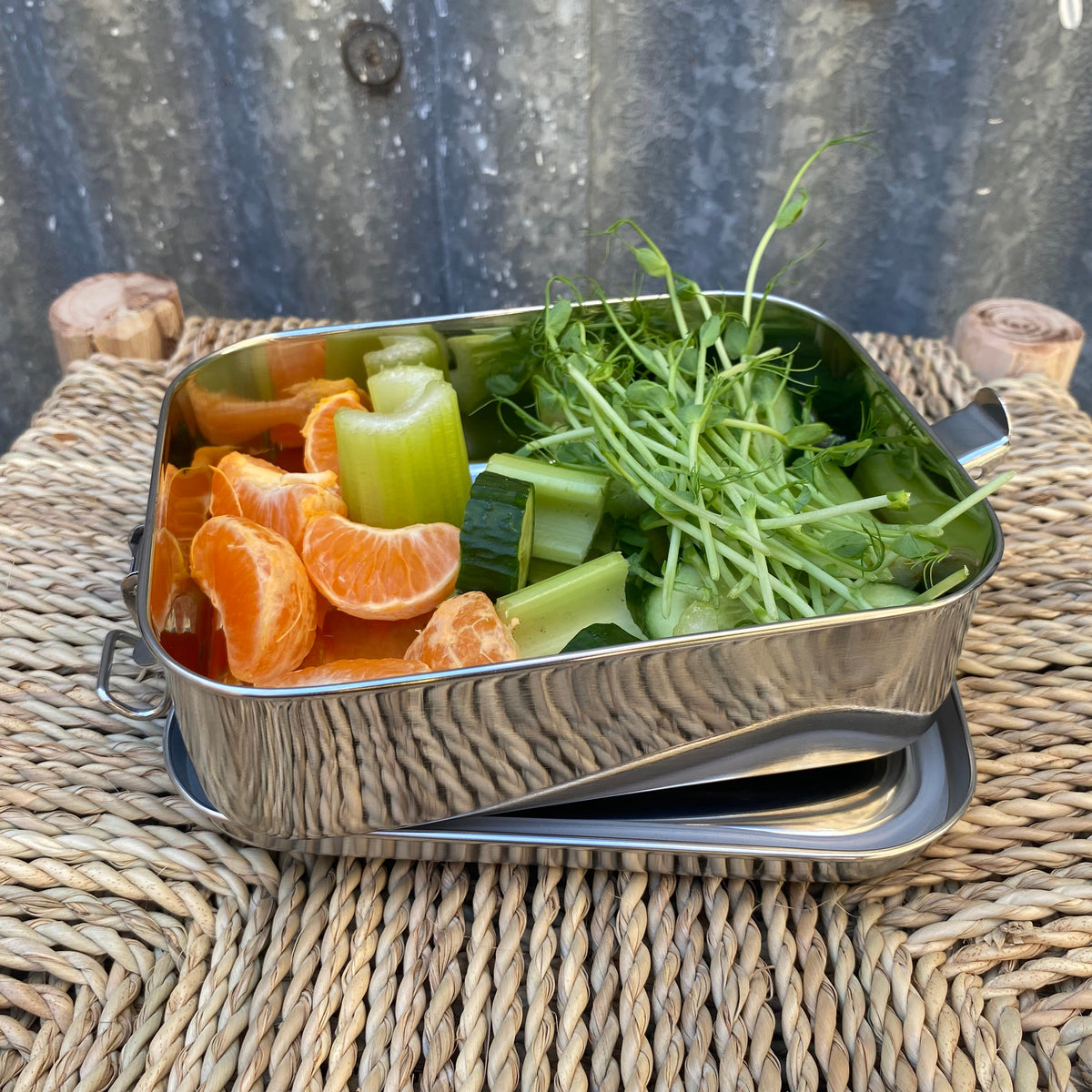 A square stainless steel lunch box with a lid. 