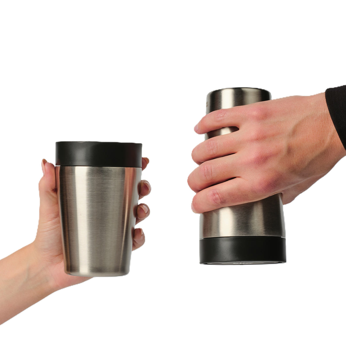 Two hands holding stainless steel travel tumblers with black lids against a plain white background.