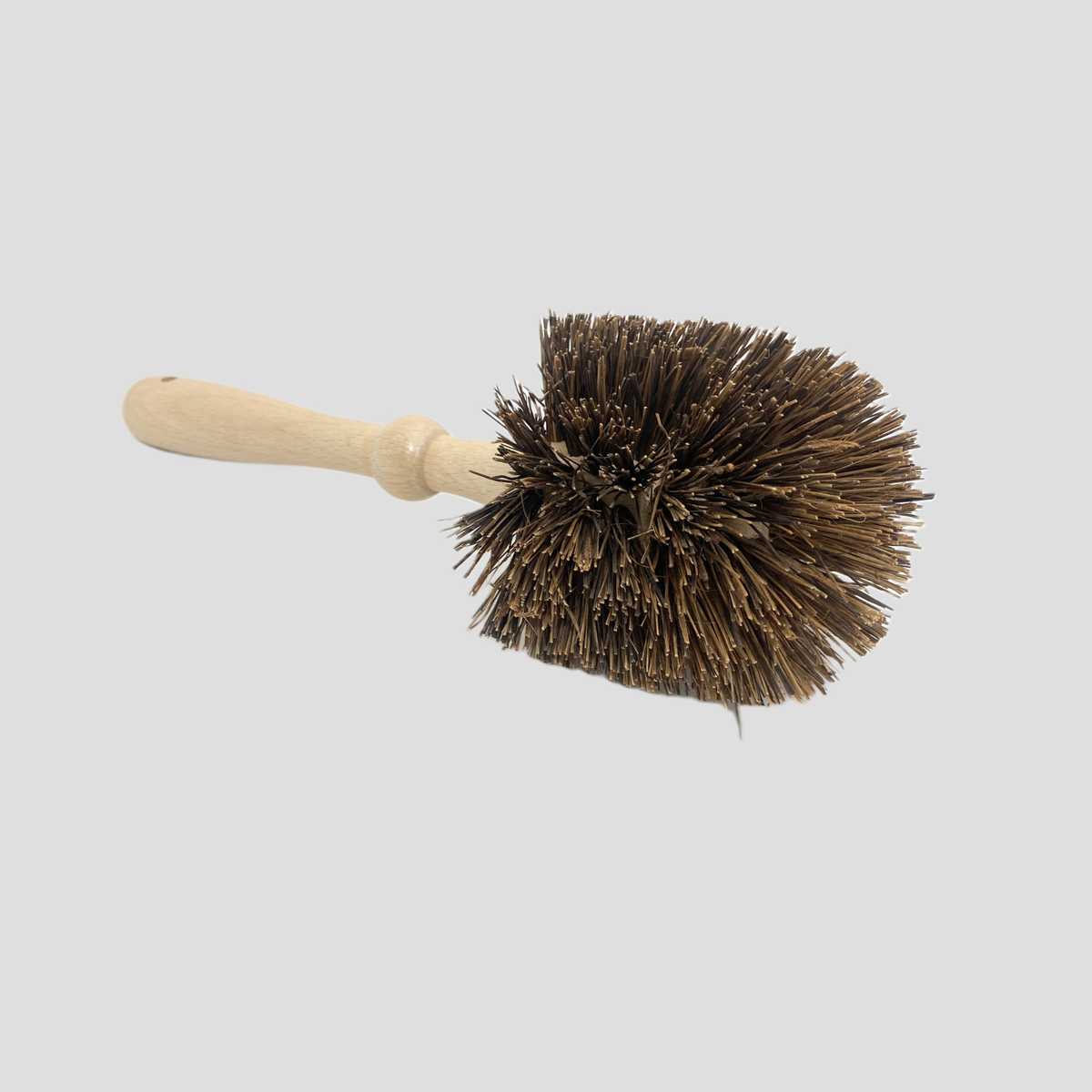 A cleaning brush with dark brown bristles and a light natural wood handle, shown against a solid light gray background.