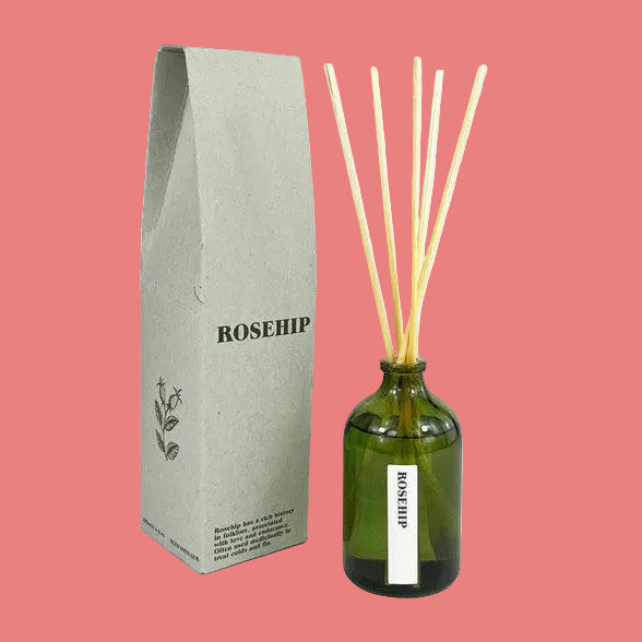 A reed diffuser set featuring an olive green glass bottle with natural wooden reeds, next to its textured light gray packaging box labeled ROSEHIP.