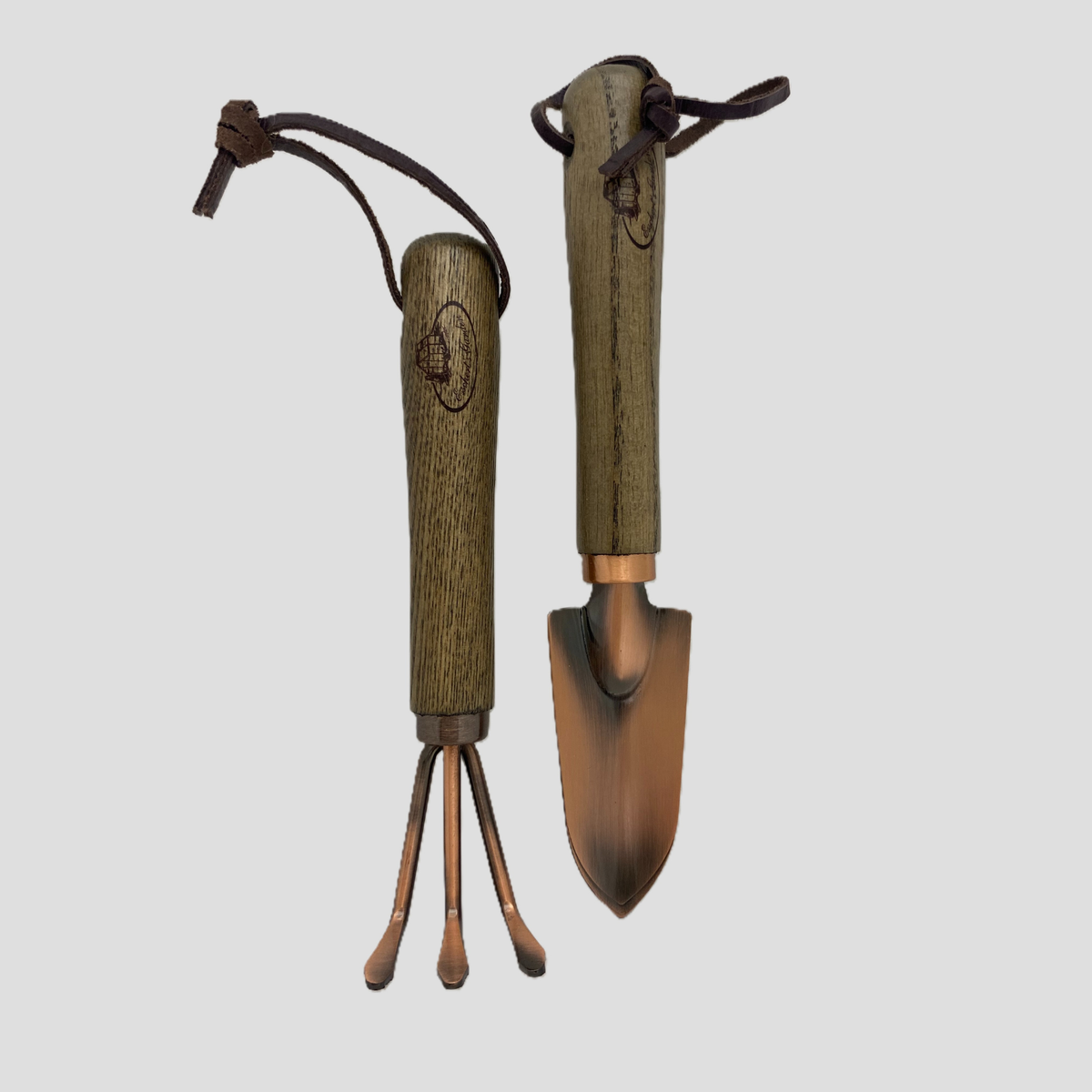 A miniature gardening tool set featuring a trowel and a three-pronged cultivator, both with dark brown faux-wood handles and bronze-colored metal heads, shown on a light gray background.