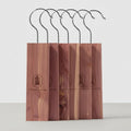 Five cedar wood bocks with black metal hooks, arranged in a row on a white background. Each stand has a vertical wood panel with a circular logo and the text 'STOCKING HANGER'.