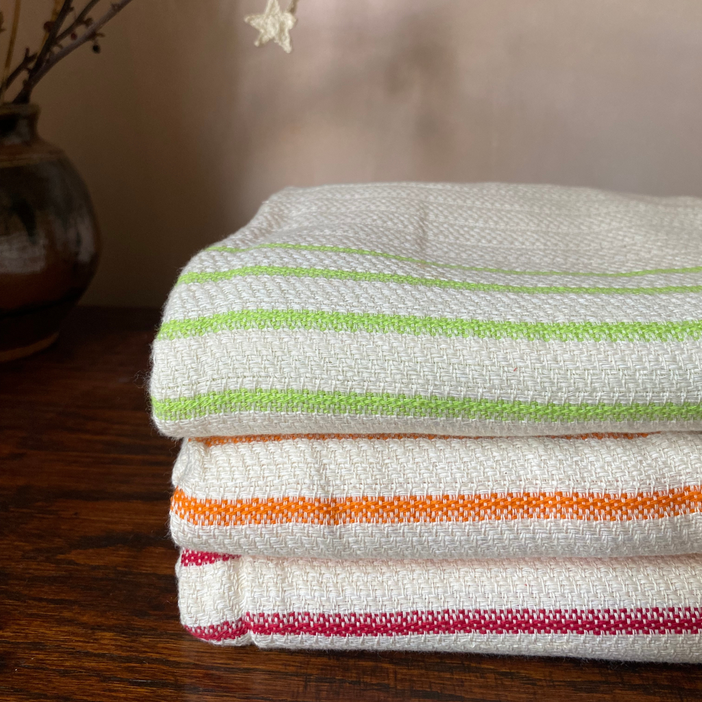 A stack of folded woven towels featuring thin horizontal stripes in green, orange, and red, displayed on a dark wooden surface.