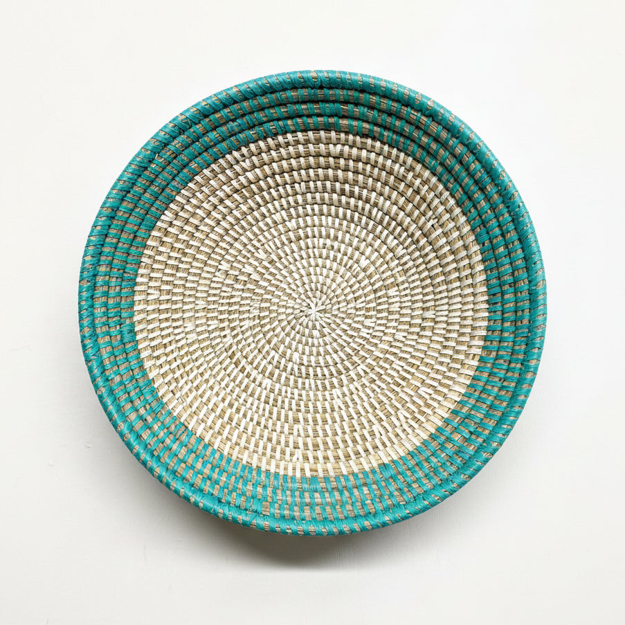 A round woven basket with a turquoise blue outer rim and a natural beige woven center, photographed from directly above on a white background.