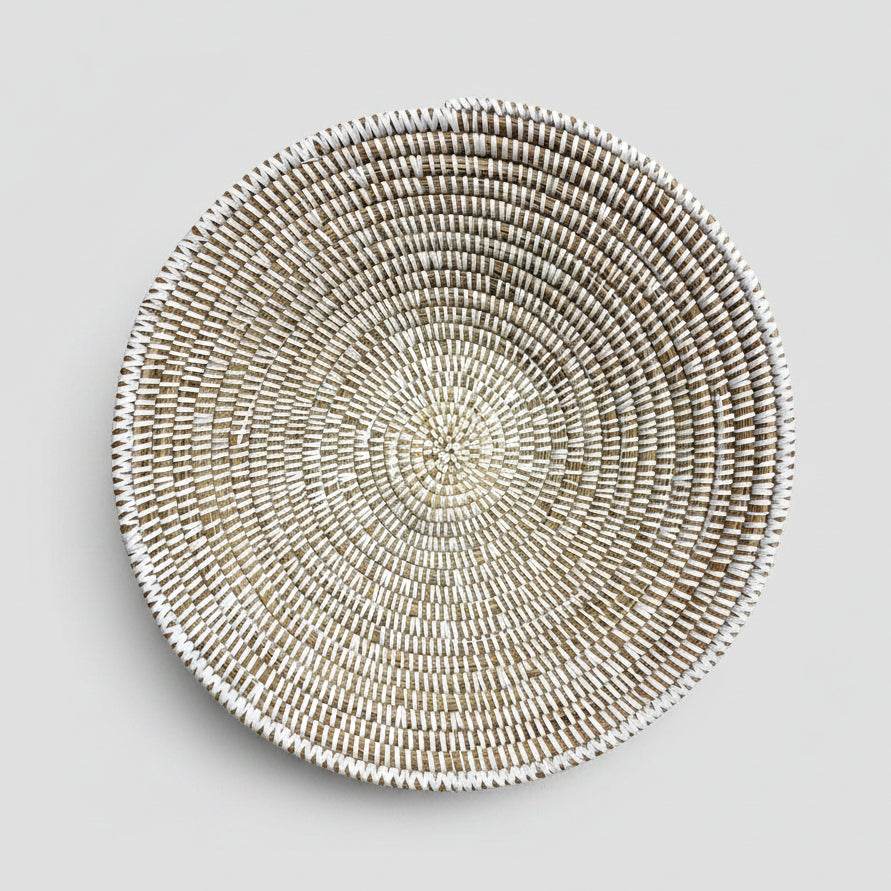 A round woven basket or tray made from natural fibers, photographed from above on a white background with a black handwritten signature reading 'La Bowl' below it.