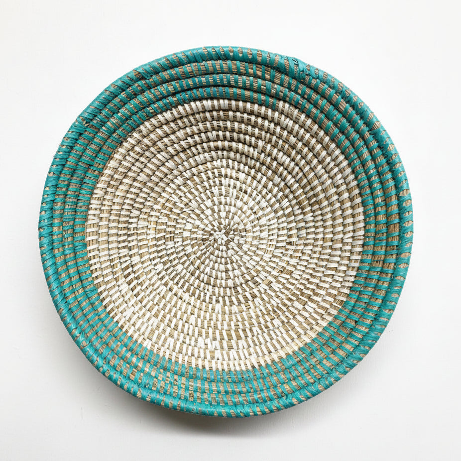 A round woven basket bowl with a turquoise and beige spiral pattern, photographed from directly above on a white background.
