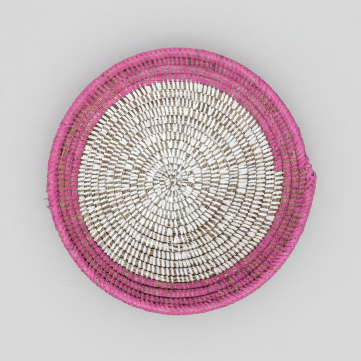 A round woven basket with a pink and white spiral pattern, photographed from directly above.