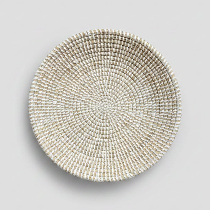 A round woven straw bowl in a light beige and white color.