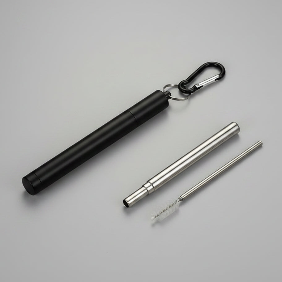 A  portable metal folding straw case. Shown on a grey surface, with a carabiner clip, plus a long metal straw and a small brush.