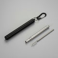 A  portable metal folding straw case. Shown on a grey surface, with a carabiner clip, plus a long metal straw and a small brush.