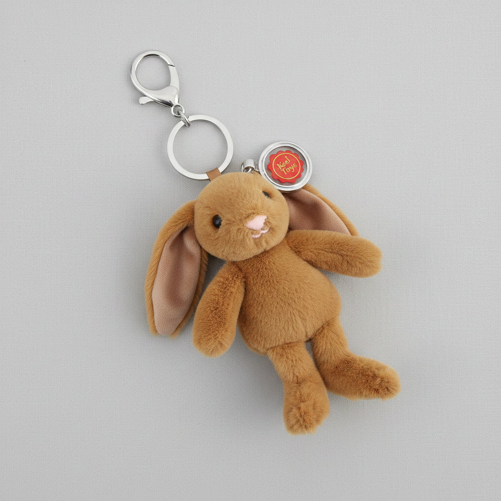 A plush brown bunny keychain with long floppy ears, a silver metal clasp, and a round red and silver tag, shown on a plain white background.