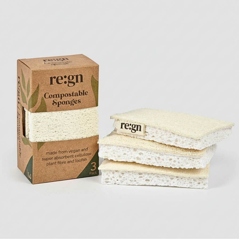 A box of Regn compostable sponges next to a stack of three natural beige loofah sponges on a white background with a faint reflection.