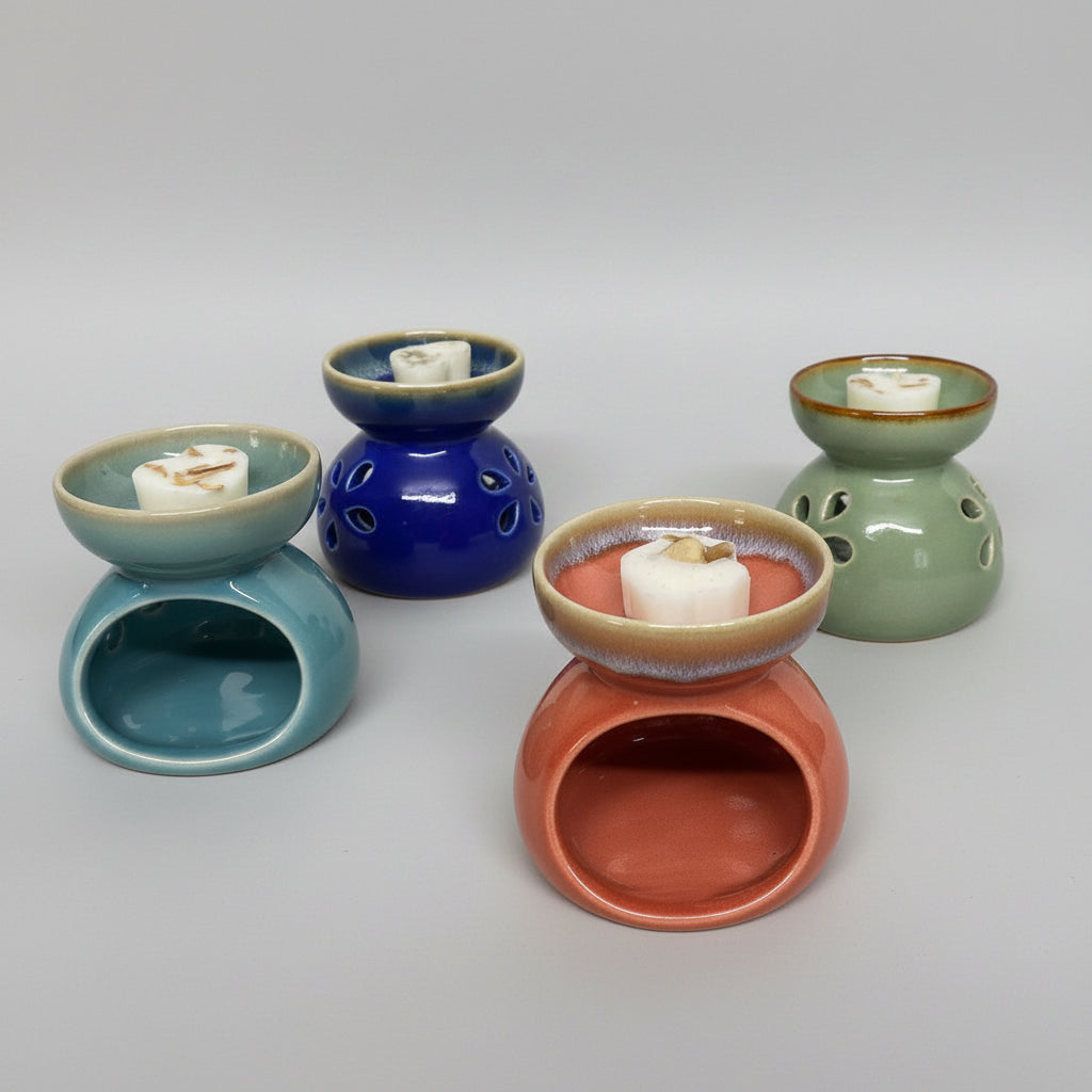 Six small ceramic wax melts or scented candle holders in assorted colors, arranged on a patterned fabric surface against a plain white wall.