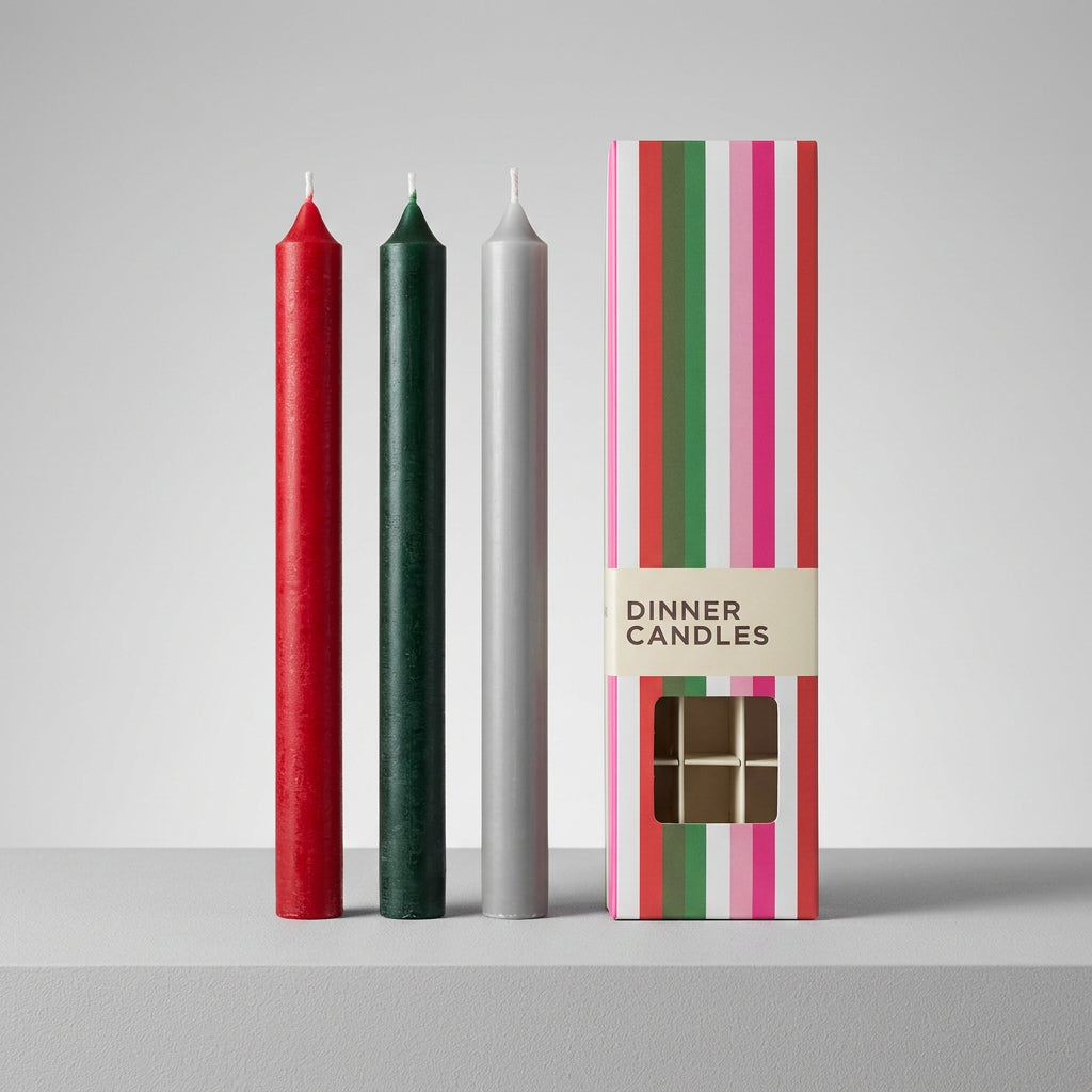 Three wax candles in red, dark green, and light gray are displayed next to their striped packaging box labeled 'DINNER CANDLES' .