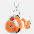 A plush clownfish keychain charm with orange and white stripes, black-tipped fins, a silver lobster clasp, and a round red-and-gold tag, shown on a plain white background.