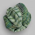 Green patterned scarf rolled up on a textured surface