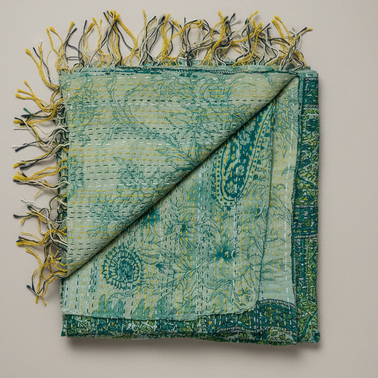 Green and beige patterned scarf with fringes on a textured white background