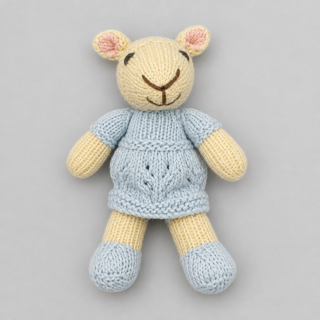 A small knitted lamb toy with a cream-colored face and arms, a light blue-gray knitted sweater, and matching light blue-gray socks, sitting against a gray knit background.