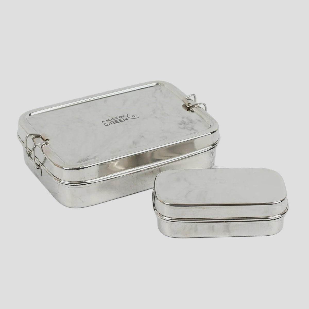 Two silver metal lidded lunch boxes, one larger tin showing the brand name 'Made by GREEN' and one smaller tin, set against a light gray background.