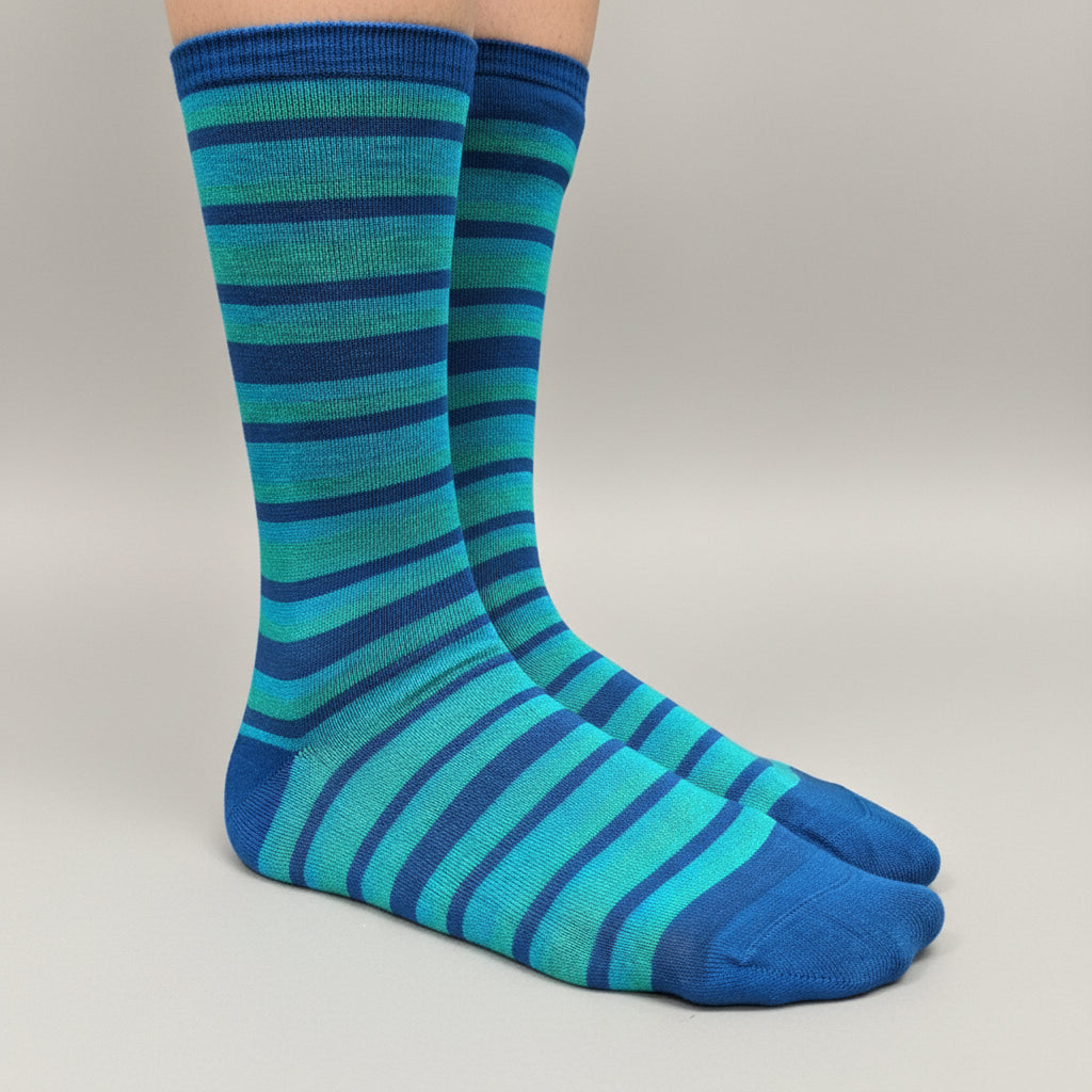 A pair of crew socks with horizontal stripes in shades of blue, teal, and turquoise, worn on a person's legs against a neutral gray studio background.