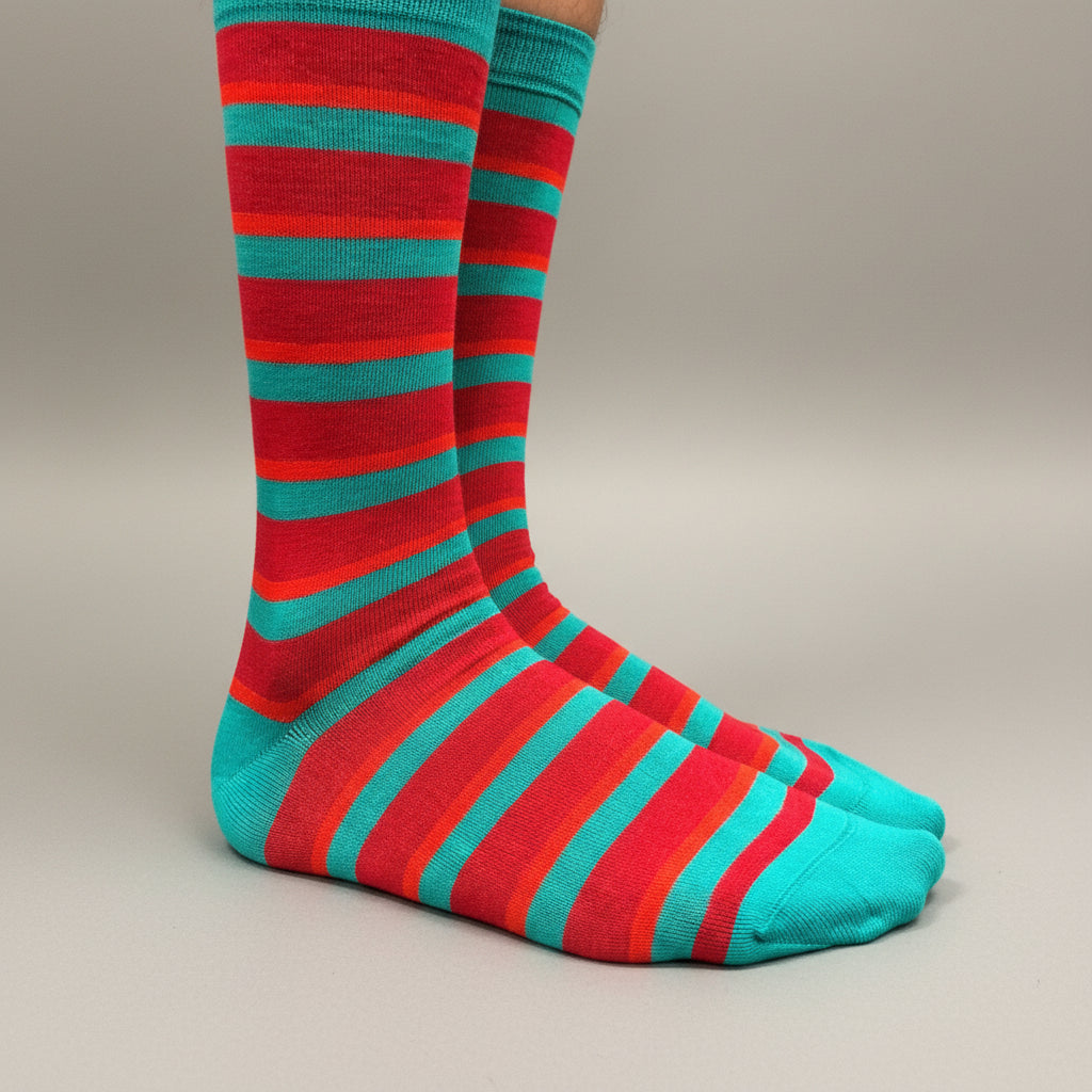 A pair of crew socks with horizontal stripes in bright red, orange, and teal, shown on a foot against a neutral gray studio background.