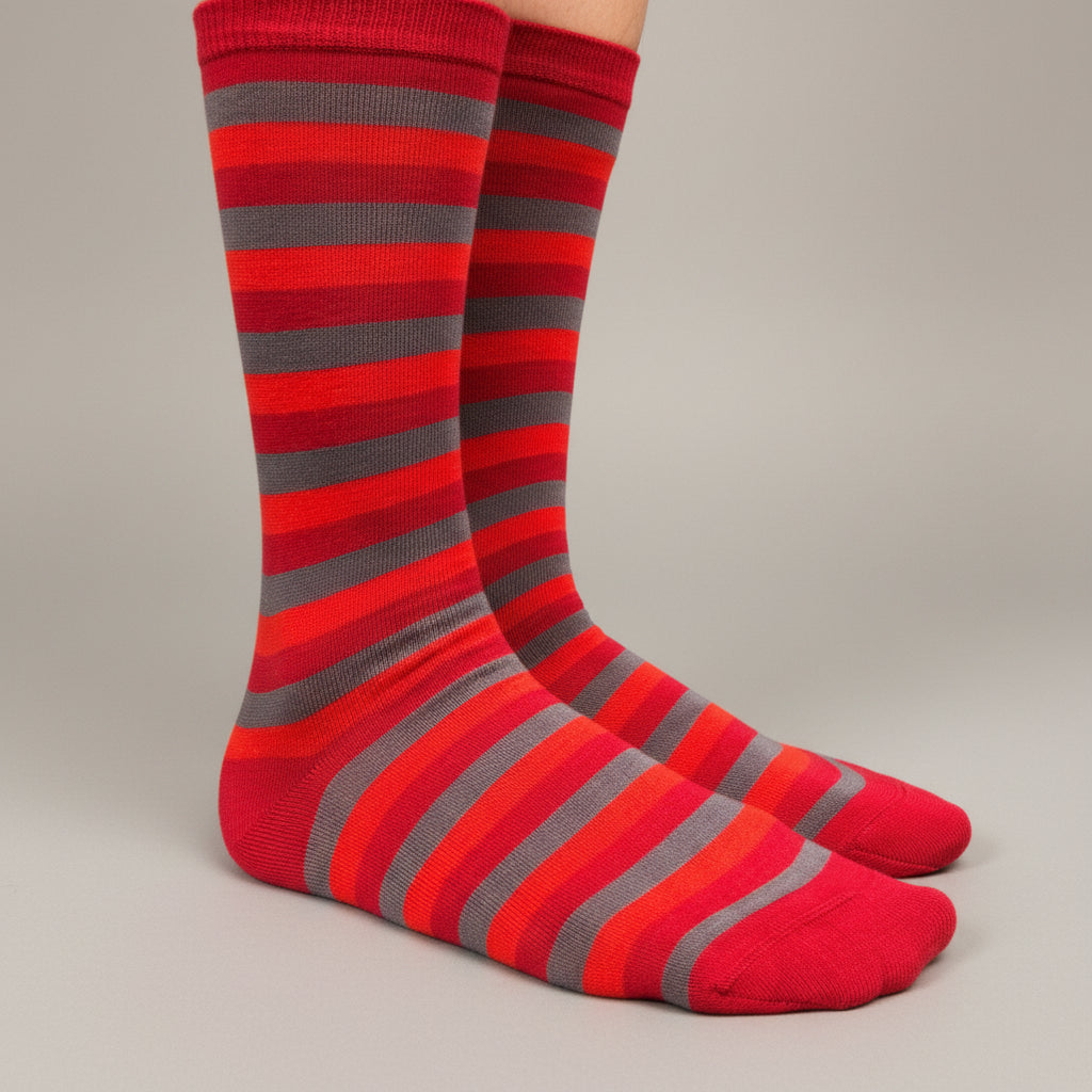 A pair of crew socks with horizontal stripes in red, orange, and gray, worn on a person's feet against a neutral gray studio background.