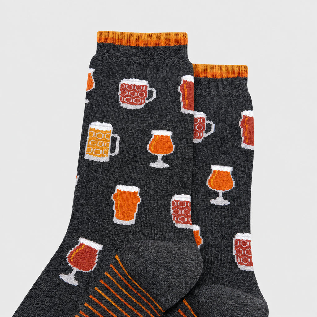 A pair of dark gray crew socks with an all-over pattern of beer mugs and pint glasses in orange, white, and brown, featuring orange and yellow striped cuffs and heels.