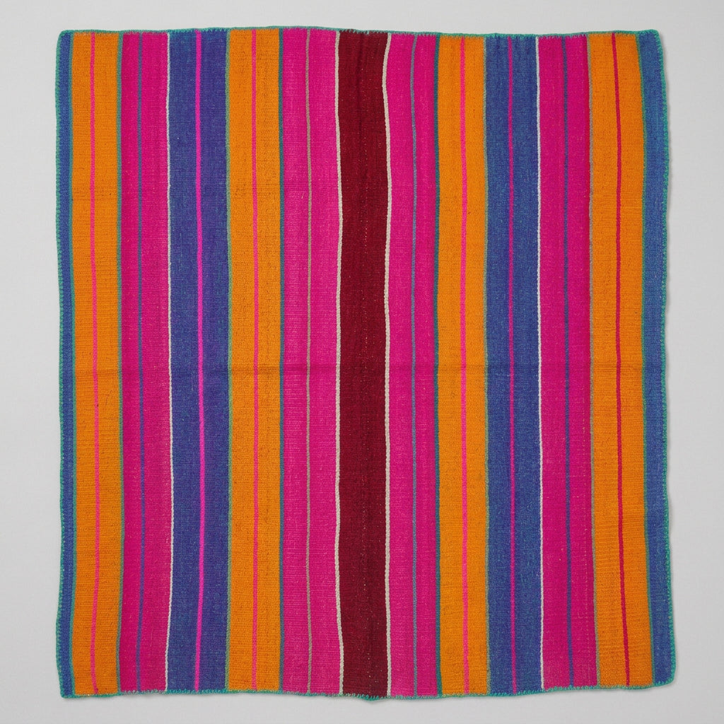 A colorful striped woven rug laid flat on a light wood floor.