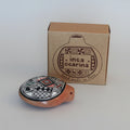 A handcrafted Inca Ocarina clay whistle with a black, red, and white geometric pattern on a terracotta base, shown in front of its brown cardboard packaging box on a white background.