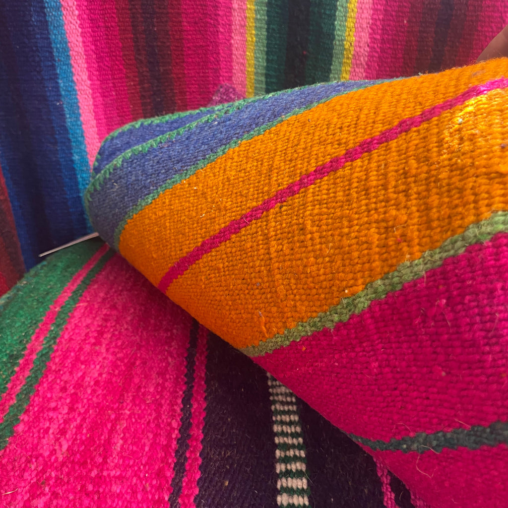 A close-up of a colorful woven textile, a peruvian serape rug , featuring bold stripes of orange, magenta pink, purple, green, and blue.