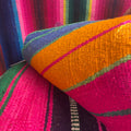 A close-up of a colorful woven textile, a peruvian serape rug , featuring bold stripes of orange, magenta pink, purple, green, and blue.