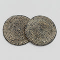 A set of two round placemats with a geometric pattern, featuring a mix of black and beige river grass with white binding.