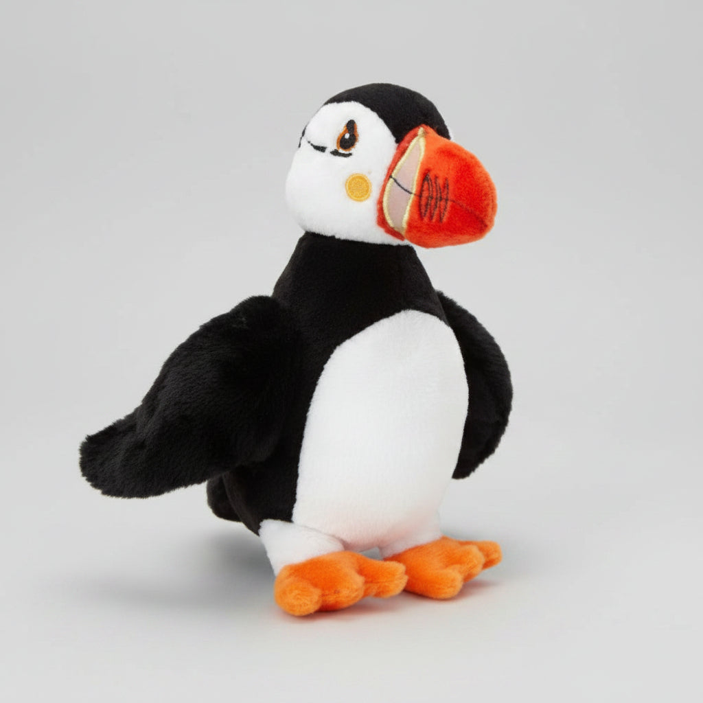 A plush puffin toy with black and white feathers, orange beak details, and orange webbed feet, photographed on a plain white background.