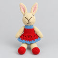 A handmade knitted bunny plush toy wearing a red dress with a blue ruffled trim and red shoes.