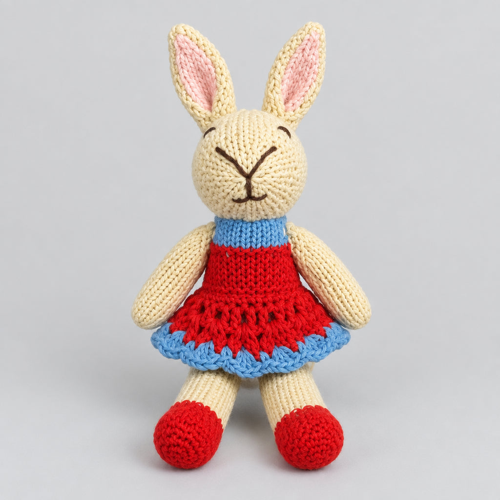 A handmade knitted bunny plush toy wearing a red dress with a blue ruffled trim and red shoes.