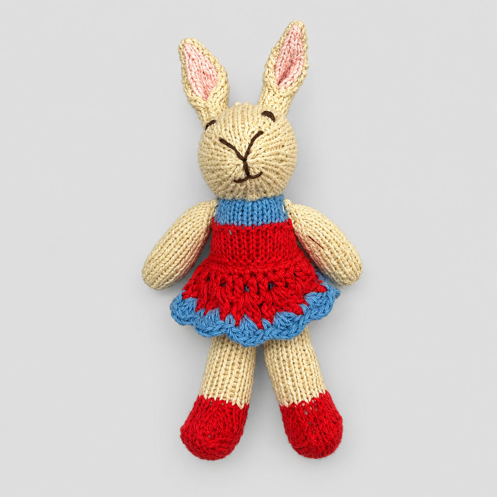A handmade knitted bunny plush toy wearing a red dress with a blue ruffled trim and red shoes.