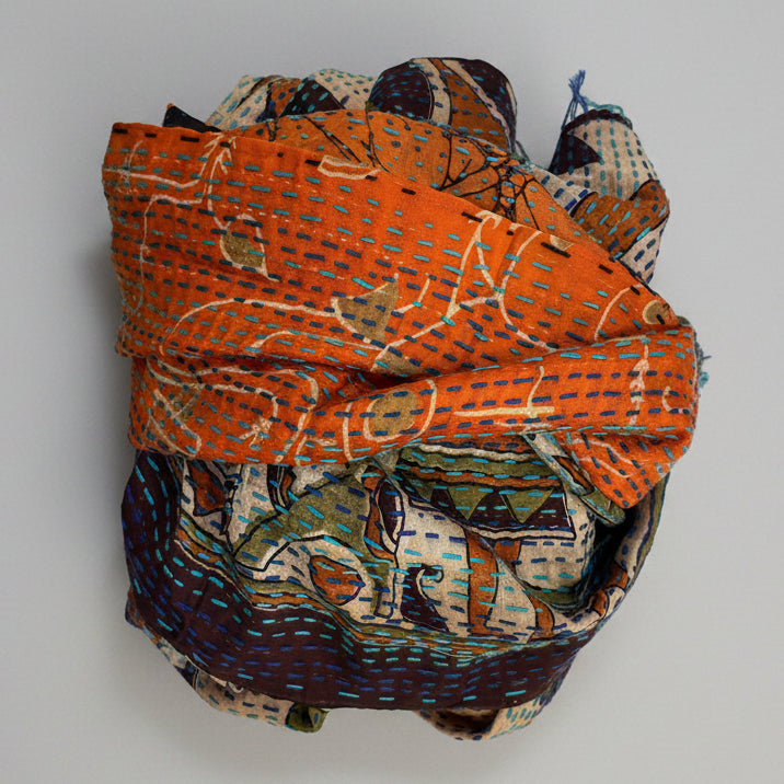 Folded scarf with orange and multicolored patterns on a grey
 background