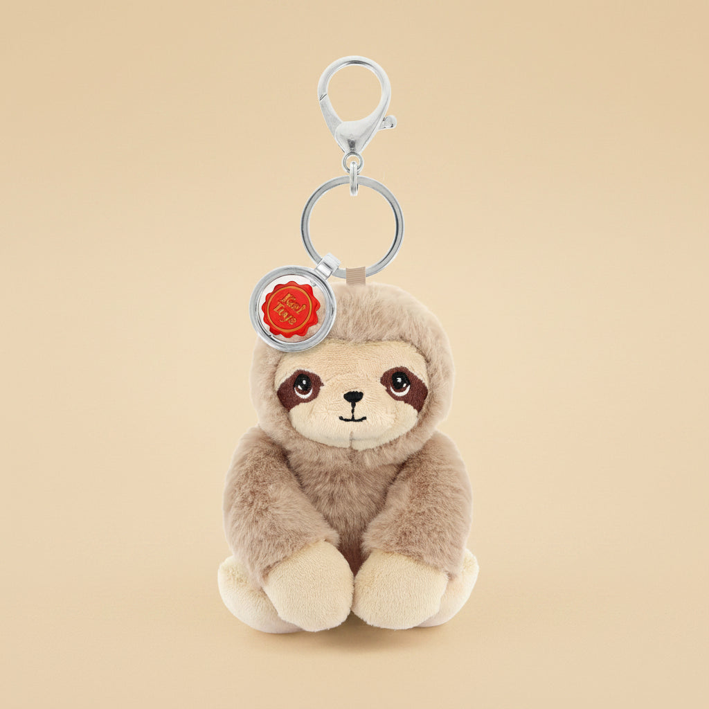 A plush sloth keychain charm with a silver metal clasp and key ring, featuring a light brown and cream sloth face with a small red circular tag.