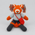 Hand-knitted red squirrel soft toy wearing a grey top, dark shorts and a red shoulder bag.”