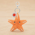 An orange plush starfish keychain with white stitched details, a silver clasp, and a small round red and gold charm, shown on a plain white background.