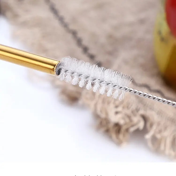A close-up of a metal cleaning brush with a gold-colored handle and white bristles, shown against a soft beige textured background.