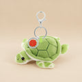 A plush green turtle keychain with a silver metal clasp and a round silver tag featuring a red seal, shown on a plain white background.