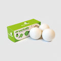 A set of three white wool dryer balls next to their green packaging box, which has the text 'Dryer Balls' and 'Pure Wool' on it.
