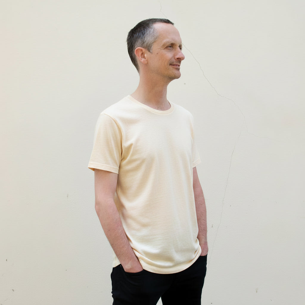 A person wearing a warm white crew neck t-shirt standing against a neutral background.